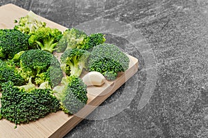 Broccoli florets and garlic cloves on wooden board. Dark background.