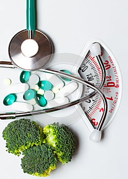 Broccoli stethoscope pills on weight scale. Dieting