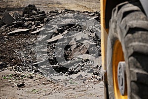 Broken asphalt on a city street next to the wheel of a heavy construction vehicle. Repair, reconstruction and danger