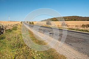 Broken asphalt road through the field at sunny day