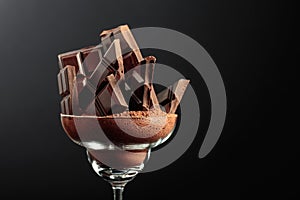 Broken black chocolate bar in glass with cocoa powder