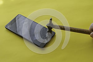 Broken black smartphone and small hammer on a yellow background