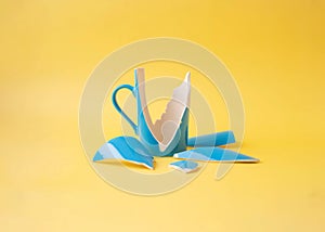 A broken blue cup with shards around on a yellow background