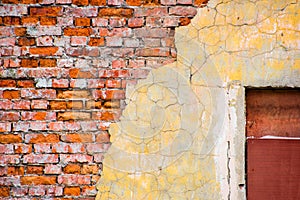 Broken brick wall with cracked plaster and a boarded up window