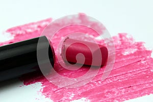 Broken bright pink lipstick lies on a white background