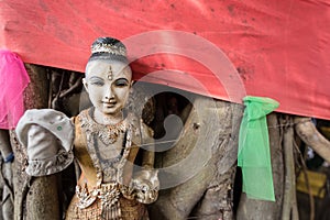 Broken Buddha statue and old religious dolls under tree in Thailand.