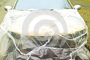 A broken car color silver, wrapped in a plastic coating. The car is covered with polyethylene after the accident. It is very debt.