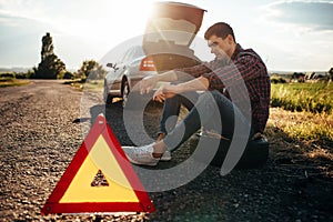 Broken car concept, man sitting on tire