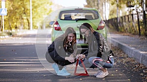 Broken car on the roadside, red warning triangle sign, driver changing flat tyre