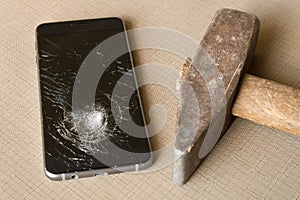 A broken cell phone and hammer on grey background
