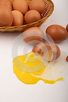 Broken chicken egg and chicken eggs in a wicker basket and eggs scattered on a white background. Close up