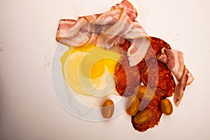 A broken chicken egg without a shell, slices of sausage and bacon and tomatoes on a white background. Close up