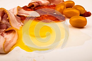 A broken chicken egg without a shell, slices of sausage and bacon and tomatoes on a white background. Close up