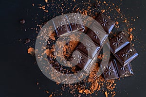 Broken chocolate bar pieces and cocoa powder on dark background