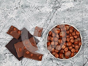 Broken chocolate bars and raw hazelnuts on gray stone background