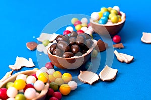 Broken chocolate easter eggs and strew colored sweets on blue background