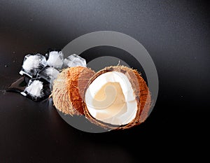 Broken coconut with white flesh and melted ice cubes on a black background