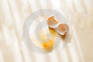 Broken and cracked brown chicken eggshell and raw egg on pastel yellow background