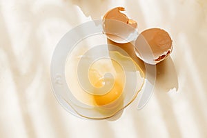 Broken and cracked brown chicken eggshell and raw egg on pastel yellow background
