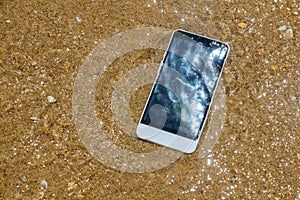 Broken crashed smartphone is lying in the water. Phone in the sandy beach