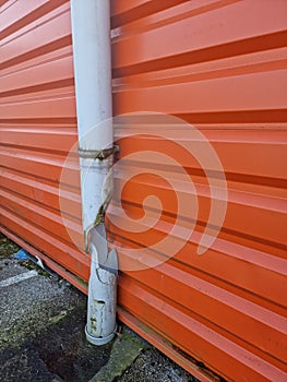 Broken damaged rain drainage pipe near red metal wall. France.