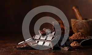 Broken dark chocolate bar and cocoa powder on a brown table