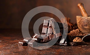 Broken dark chocolate bar and cocoa powder on a brown table