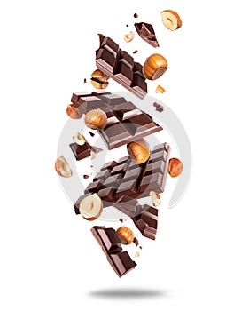 Broken dark chocolate bar with hazelnuts in the air isolated on a white background