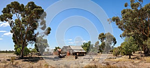 A broken decaying old timber farmers workers home surrounded by native trees on a dry barren agricultural proper