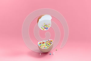 Broken decorative easter egg with colorful confetti. Minimal composition, vivid color pastel pink background. Copy space