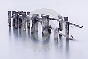 Broken down old pier posts in calm water, covered with light dusting of snow