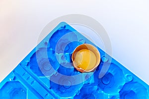 Broken egg in a bright yellow container. White abstract background.