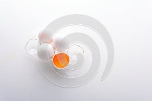 Broken egg with whole eggs in a transparent plastic container on white wooden background