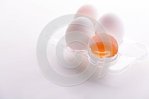 Broken egg with whole eggs in a transparent plastic container on white wooden background