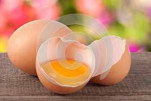 Broken egg with yolk and eggshell On a wooden table with a blurry garden background