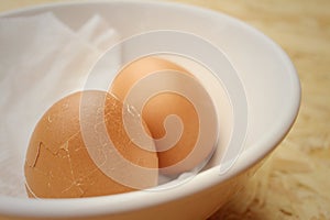 Broken eggs in white bowl on wooden background.