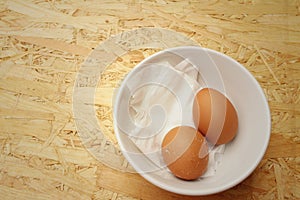 Broken eggs in white bowl on wooden background.