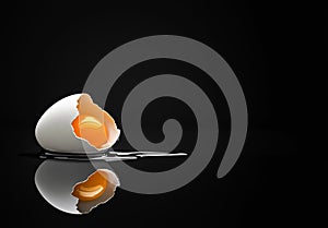 Broken eggshell with raw egg on a black minimalist surface reflective background
