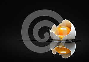 Broken eggshell with raw egg on a black minimalist surface reflective background