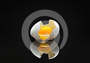 Broken eggshell with raw egg on a black minimalist surface reflective background