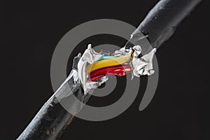 Broken electric cord with red and electric yellow wires intertwined. Damaged power electrical cable on black background, close up