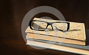 a broken eyeglass frame lies on a stack of old books on a brown wooden table