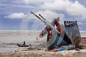 Broken fishing boat wreckage on a sandy beach under bad weather