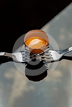 Broken fresh chicken egg Hen egg balanced on a composition of two intertwined forks over black floor