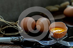 Broken fresh chicken egg Hen egg balanced on a composition of two intertwined forks and Two fresh chicken eggs over black floor