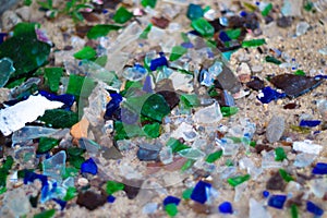 Broken glass bottles on white sand. Bottles is green and blue colour. Trash on the sand. Ecological problem