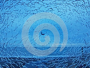 Broken glass with cracks. Abstract cracked shot window on blue