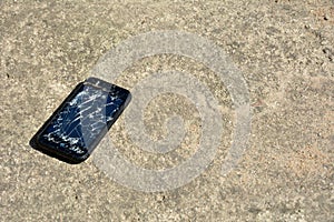 Broken glass of mobile phone screen on concrete floor. Black Smartphone on cement floor