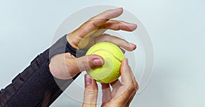 Broken hand in black orthosis holding a yellow tennis ball for training and recovery on light gray background