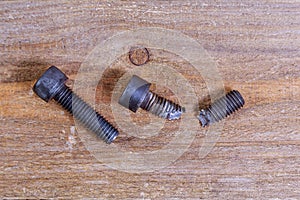 Broken hardened black bolts on a wooden background.